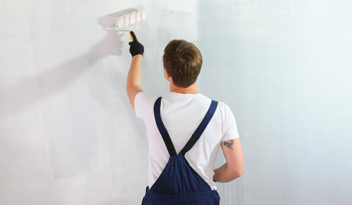 Young worker painting wall in room